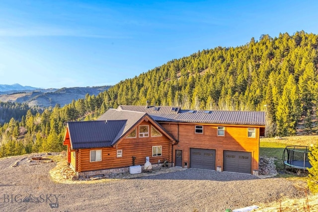 log-style house with a garage, a trampoline, driveway, and a view of trees