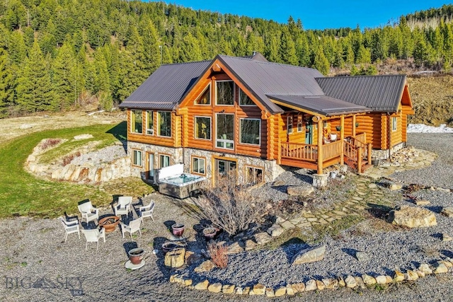 rear view of property with metal roof, log siding, a wooded view, a fire pit, and stone siding