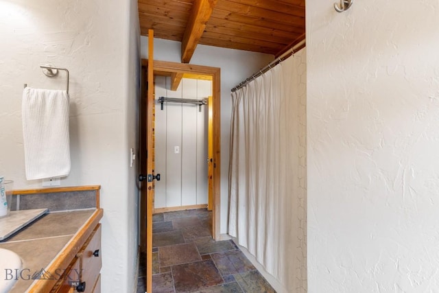 bathroom featuring wood ceiling, beam ceiling, vanity, and stone tile flooring