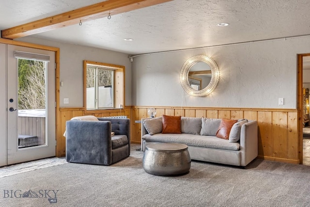 carpeted living room with a wainscoted wall, beamed ceiling, wood walls, and a textured ceiling