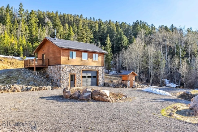 exterior space with an attached garage, stone siding, a view of trees, driveway, and metal roof