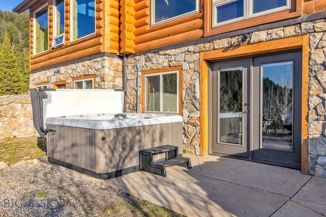 entrance to property with a patio, log siding, a hot tub, and stone siding