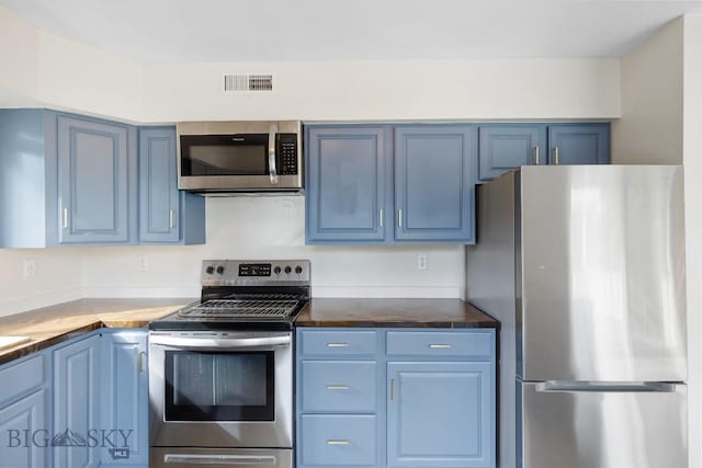 kitchen with dark countertops, stainless steel appliances, blue cabinets, and visible vents