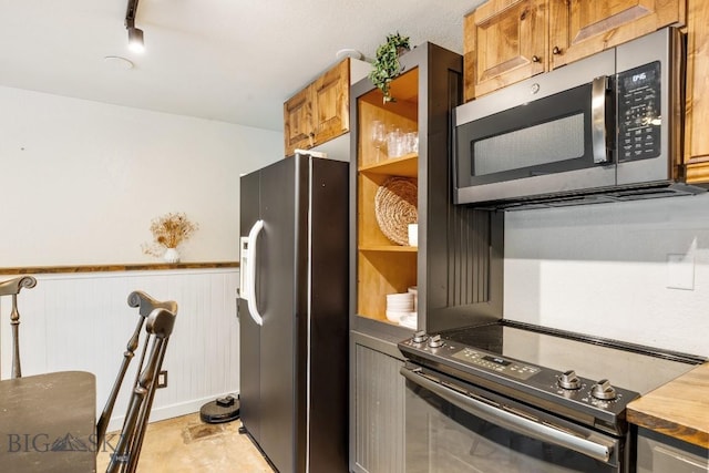 kitchen featuring black electric range, brown cabinets, fridge with ice dispenser, a wainscoted wall, and stainless steel microwave