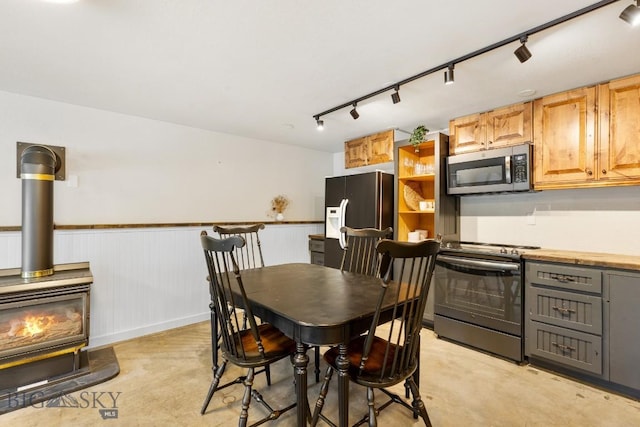 dining area featuring wainscoting, rail lighting, a wood stove, and concrete floors