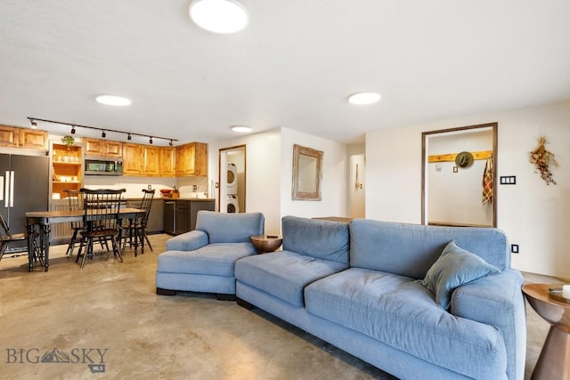 living room featuring stacked washing maching and dryer, track lighting, and finished concrete floors