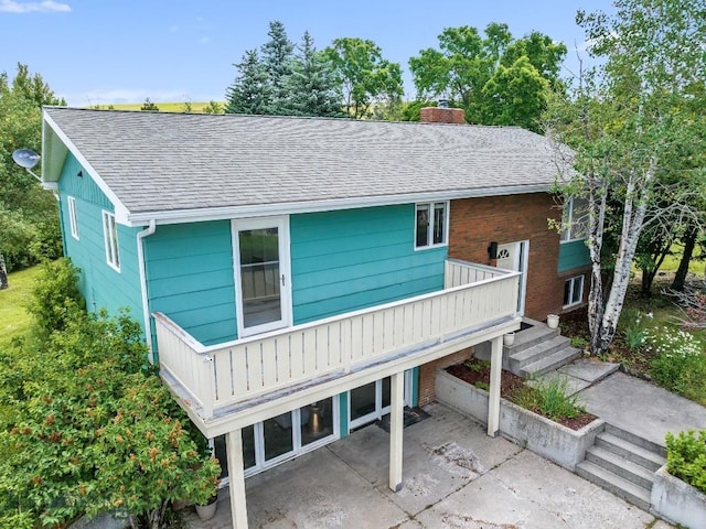 exterior space featuring a patio, a shingled roof, and a chimney