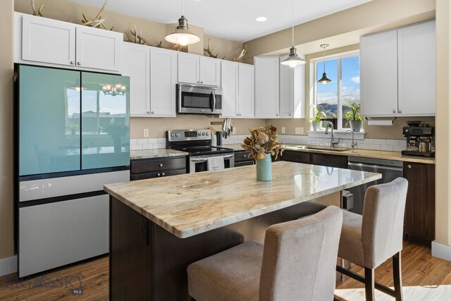 1604 Drummond Blvd, Belgrade, MT 59714 - kitchen with decorative light fixtures, appliances with stainless steel finishes, a center island, light stone countertops, and a sink