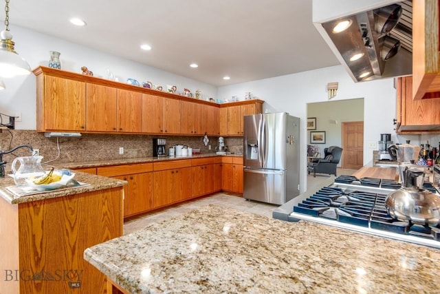 kitchen with brown cabinetry, backsplash, light stone counters, stainless steel fridge, and extractor fan