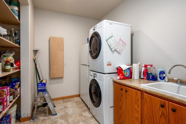 washroom featuring cabinet space, baseboards, a sink, and stacked washer and clothes dryer