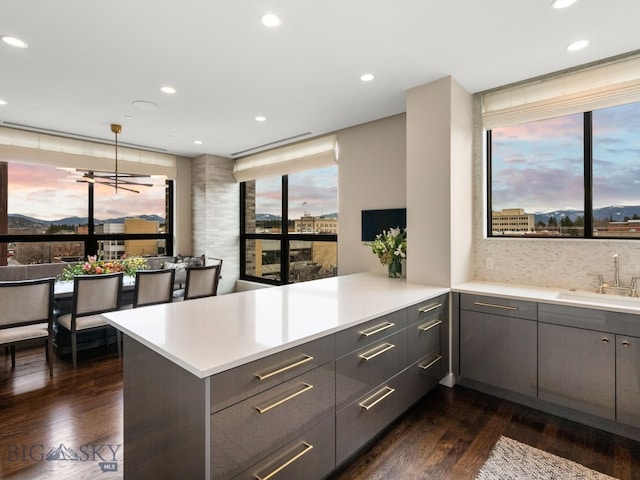 kitchen featuring a peninsula, dark wood-type flooring, recessed lighting, gray cabinets, and a sink