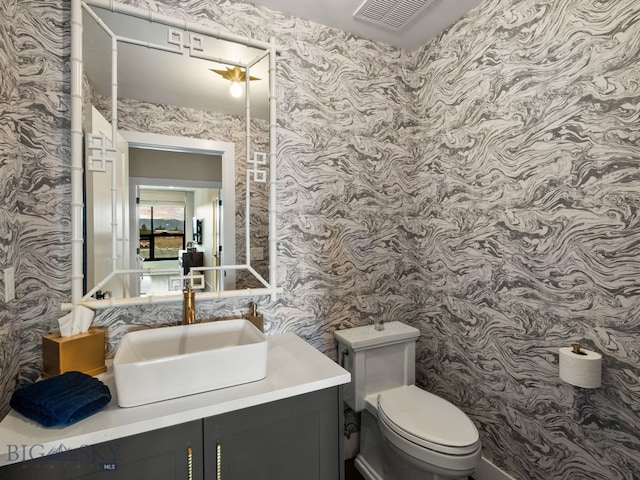 half bathroom featuring toilet, wallpapered walls, visible vents, and vanity
