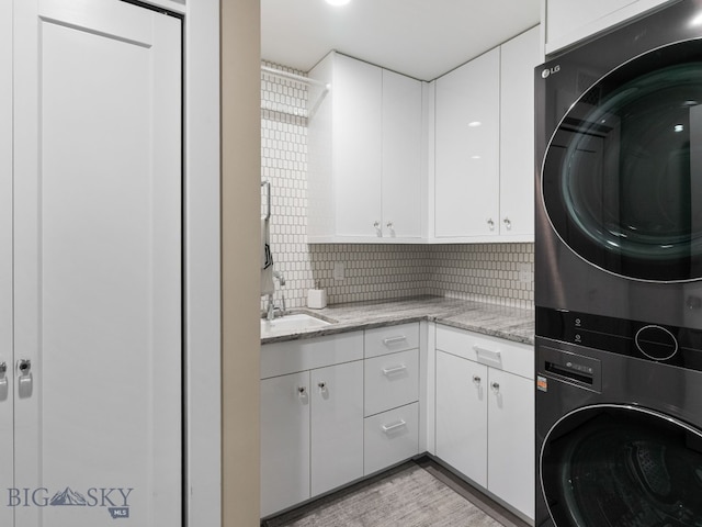 laundry room featuring cabinet space, light wood-style flooring, a sink, and stacked washer and clothes dryer