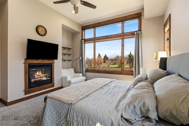 carpeted bedroom with baseboards, a ceiling fan, and a glass covered fireplace