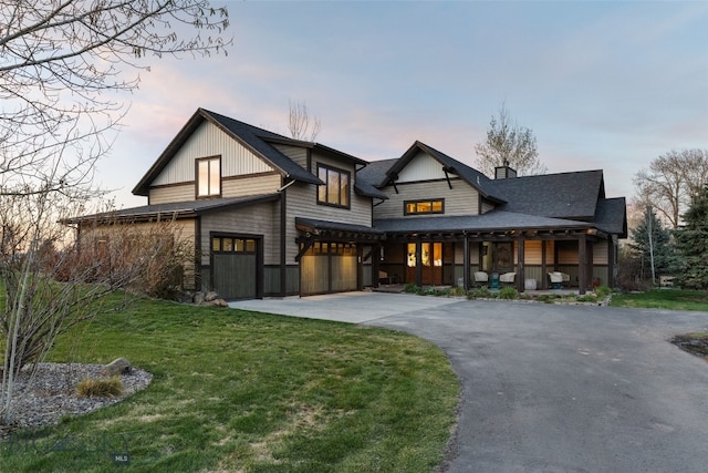 modern farmhouse style home with an attached garage, aphalt driveway, a chimney, a porch, and a yard