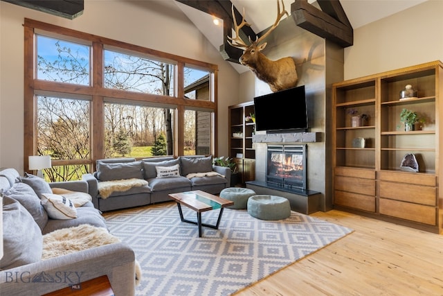 living room featuring light wood-style floors, high vaulted ceiling, a glass covered fireplace, and a wealth of natural light