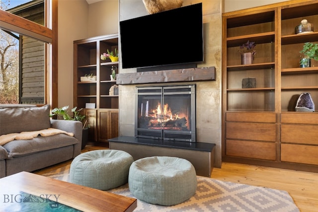 living area featuring a lit fireplace, built in features, and wood finished floors