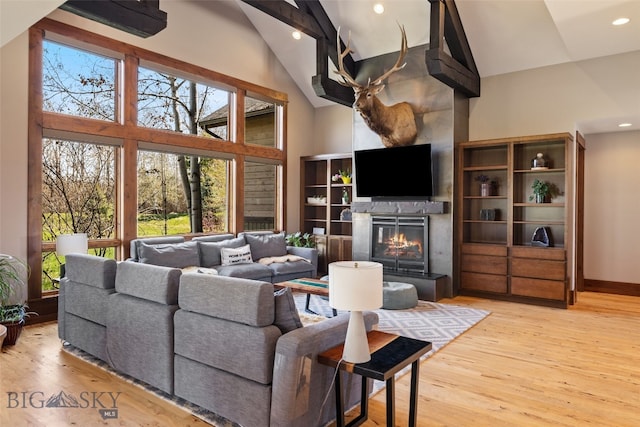 living room featuring recessed lighting, high vaulted ceiling, a glass covered fireplace, and light wood-style flooring