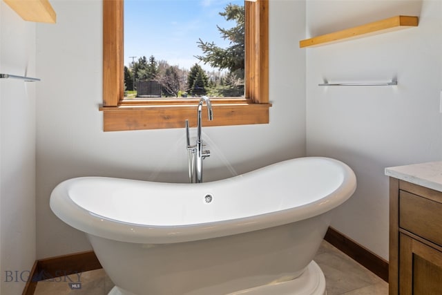 full bathroom with a freestanding tub, vanity, and baseboards