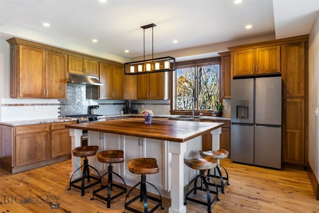 kitchen with brown cabinets, a sink, stainless steel fridge with ice dispenser, wood counters, and under cabinet range hood