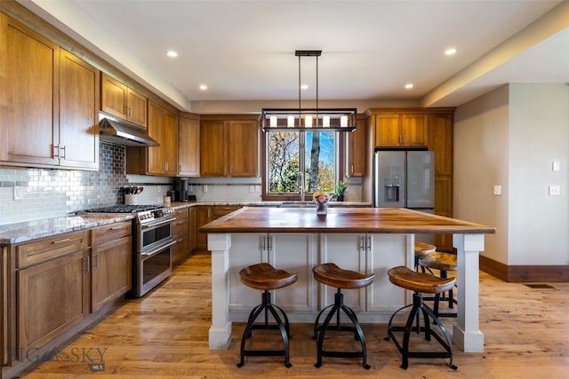 kitchen with butcher block counters, a kitchen island, under cabinet range hood, tasteful backsplash, and appliances with stainless steel finishes