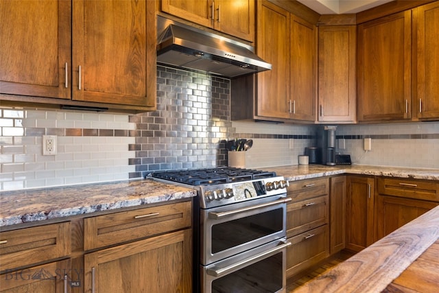 kitchen featuring tasteful backsplash, under cabinet range hood, and range with two ovens