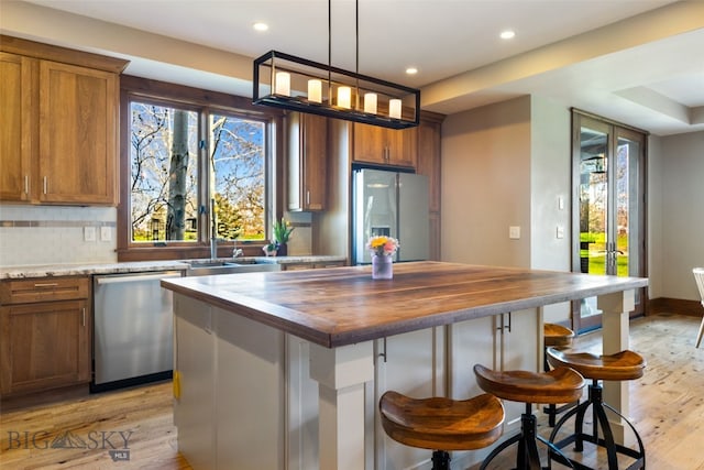 kitchen with light wood finished floors, recessed lighting, brown cabinets, wood counters, and appliances with stainless steel finishes