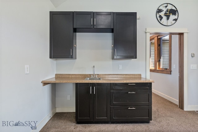 kitchen with carpet floors, a sink, dark cabinetry, and baseboards