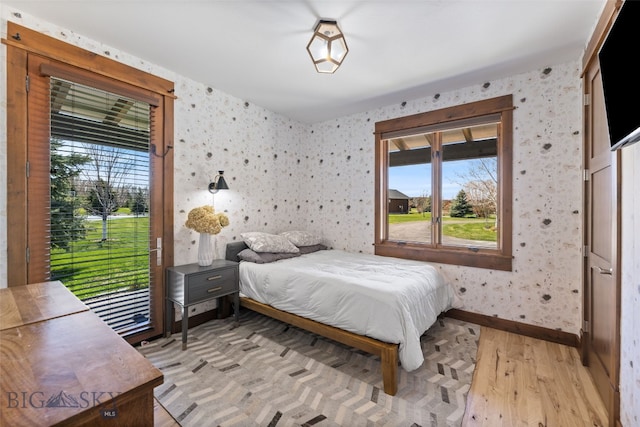 bedroom with wallpapered walls, multiple windows, baseboards, and light wood-style floors