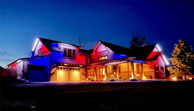 back of house at night featuring a garage and driveway
