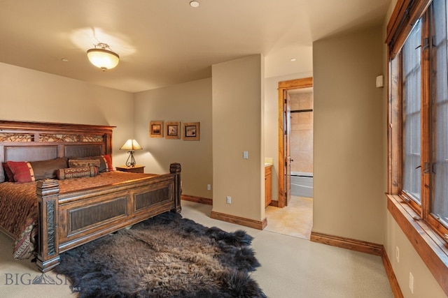 bedroom with baseboards, ensuite bathroom, and light carpet