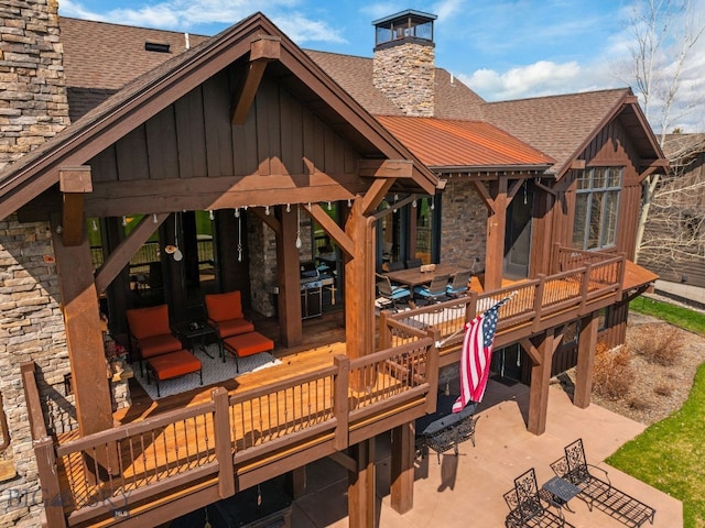 exterior space with a shingled roof, stone siding, board and batten siding, a chimney, and a patio