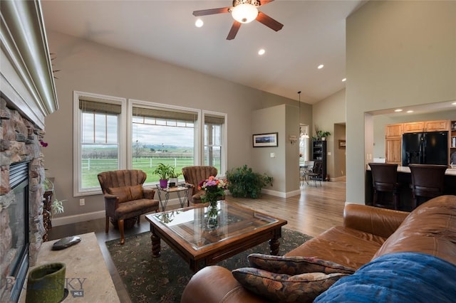 living area featuring plenty of natural light, light wood-style flooring, ceiling fan, and a stone fireplace