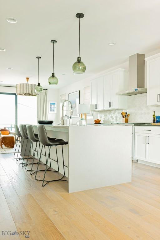 kitchen featuring a kitchen breakfast bar, backsplash, light wood-type flooring, white cabinets, and wall chimney exhaust hood
