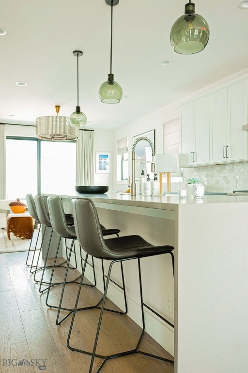 kitchen featuring white cabinets, hanging light fixtures, light countertops, a kitchen breakfast bar, and light wood-type flooring