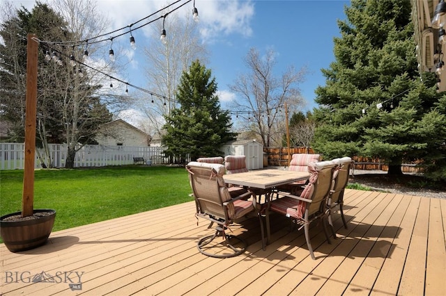 deck with a lawn, outdoor dining area, a fenced backyard, and a shed