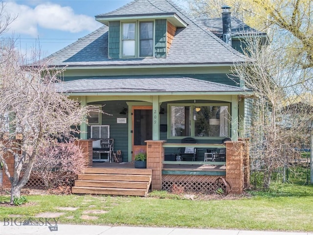 view of front of home featuring covered porch, a shingled roof, and a front yard