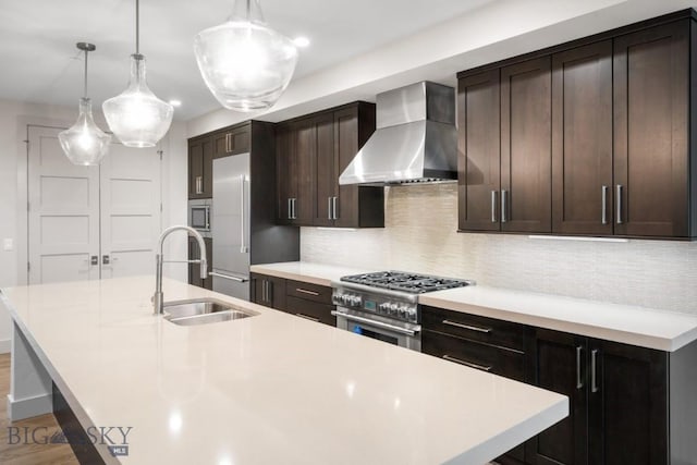 kitchen with wall chimney range hood, appliances with stainless steel finishes, a sink, an island with sink, and decorative backsplash