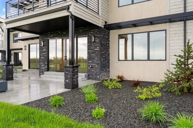 doorway to property featuring a balcony, stone siding, and stucco siding