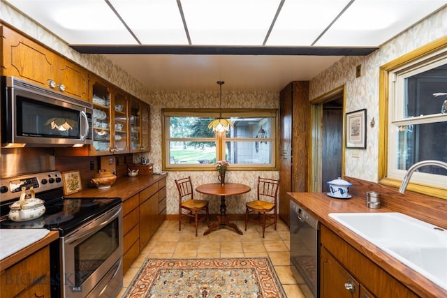 423 Riverview Ct, Great Falls, MT 59404 - kitchen featuring brown cabinets, appliances with stainless steel finishes, a sink, wallpapered walls, and glass insert cabinets