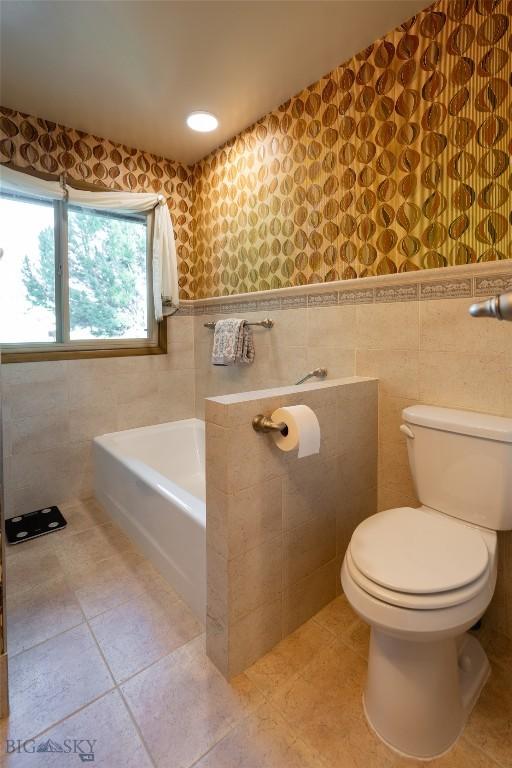 423 Riverview Ct, Great Falls, MT 59404 - bathroom featuring a bath, toilet, tile walls, and tile patterned flooring