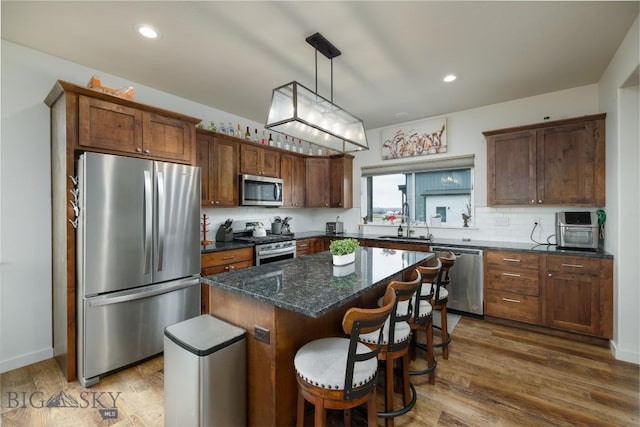 kitchen featuring appliances with stainless steel finishes, decorative backsplash, a kitchen island, and wood finished floors