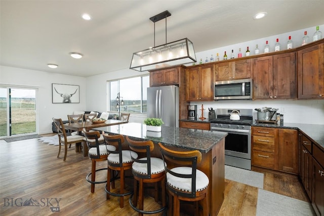 kitchen featuring a breakfast bar area, a kitchen island, dark wood-style flooring, decorative light fixtures, and appliances with stainless steel finishes