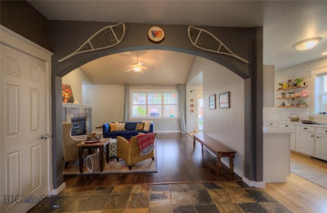 living room with arched walkways, a ceiling fan, wood finished floors, and a tile fireplace