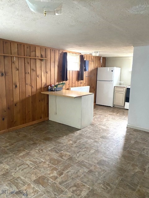 kitchen with a textured ceiling, wood walls, light countertops, freestanding refrigerator, and a peninsula