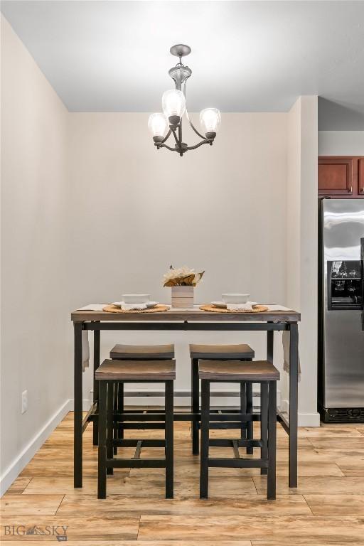 dining space with baseboards, light wood finished floors, and a notable chandelier