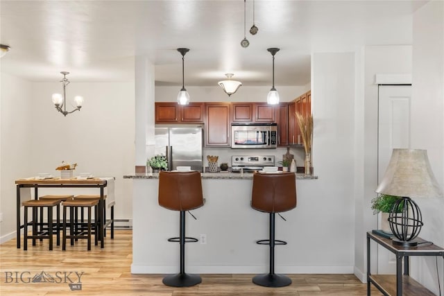 kitchen with a peninsula, a breakfast bar, light wood-style floors, dark stone countertops, and appliances with stainless steel finishes