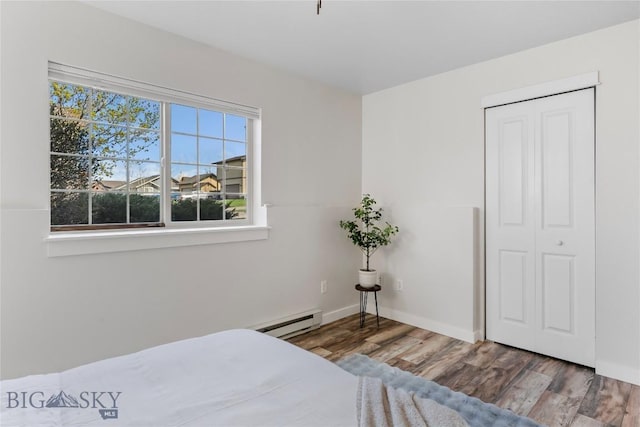 bedroom with wood finished floors, baseboards, a baseboard heating unit, and a closet