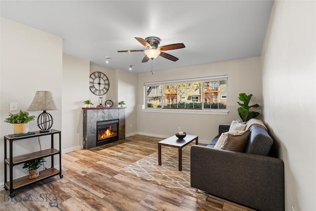living room featuring baseboards, ceiling fan, a fireplace, and wood finished floors