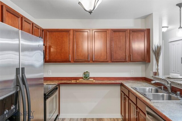 kitchen featuring brown cabinetry, a sink, appliances with stainless steel finishes, and hanging light fixtures